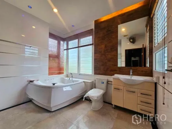 Detached House for rent in Chatuchak, Bangkok - Bright master bathroom with corner jacuzzi tub, wood accent wall, vanity and large windows.