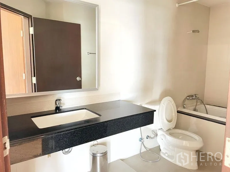 Condominium for rent in Khlong Toei, Bangkok - Bathroom with long black vanity, mirror, toilet and bathtub with shower.