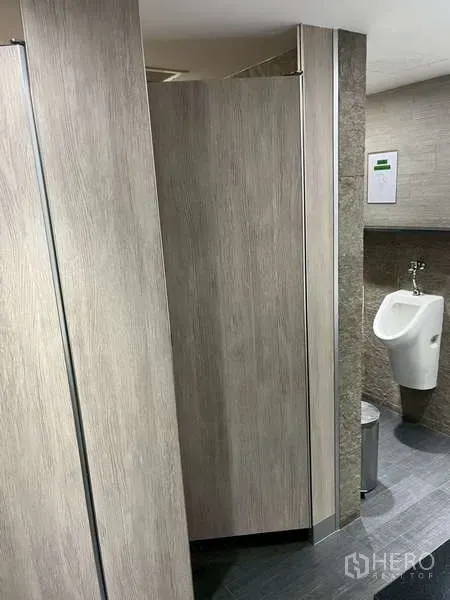 Office Space for rent - Men’s restroom with partitioned stalls and a wall-mounted urinal.