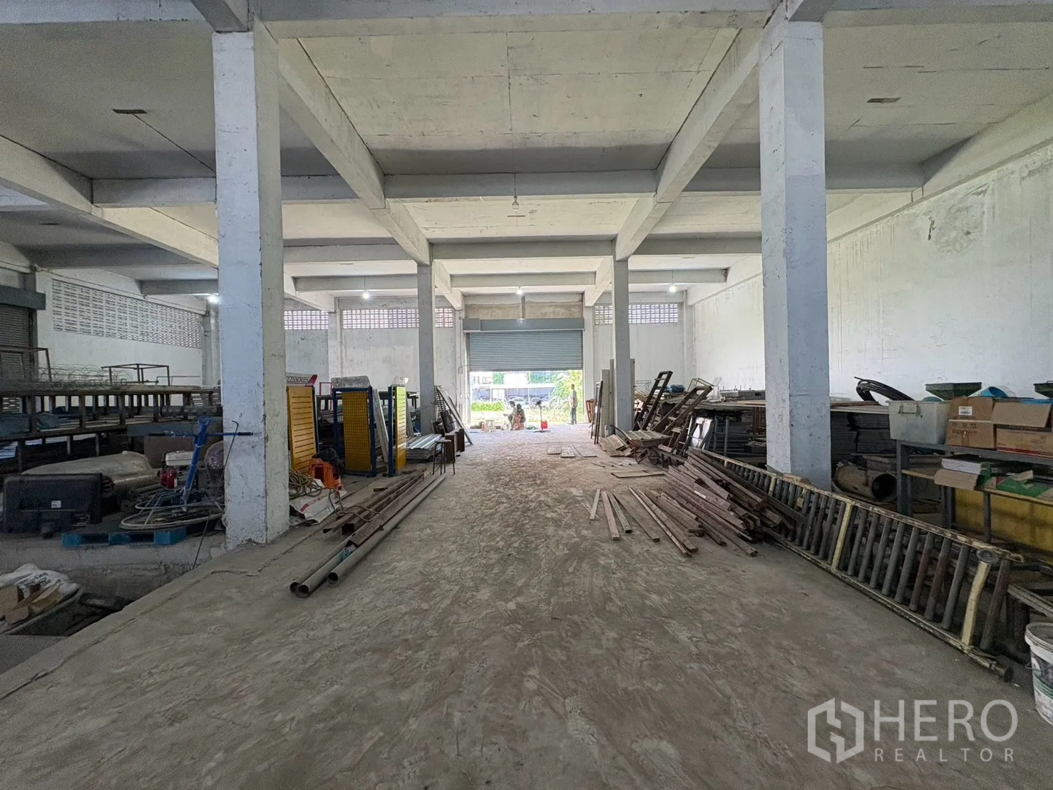 Warehouse for rent in Bang Na, Bangkok - Wide warehouse aisle with concrete floor, columns, and a roll-up door at the far end.
