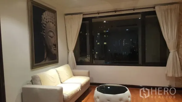 公寓 出租在Sathon, Bangkok - 起居区配米色沙发、佛像艺术画与大窗，远眺城市灯火。