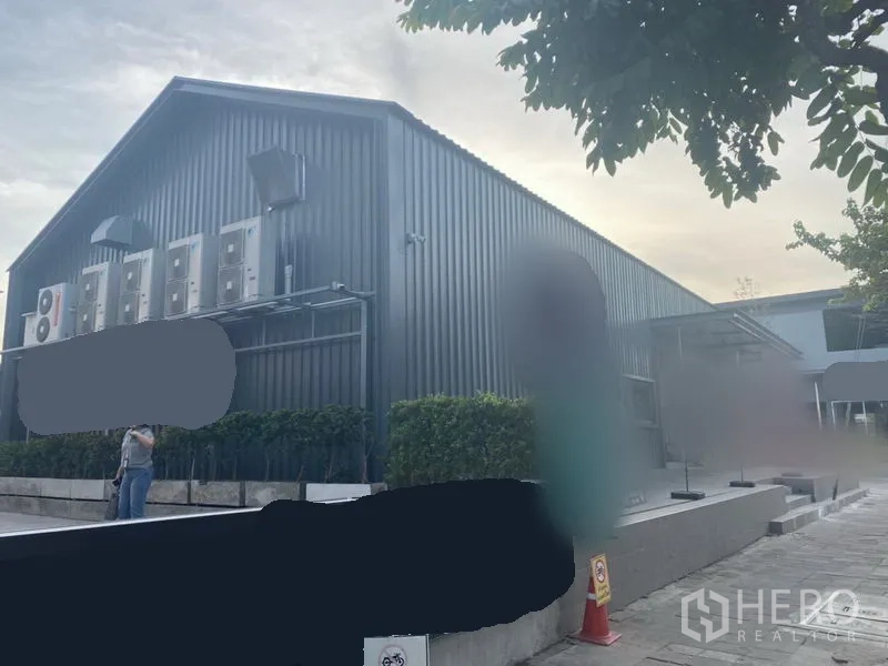 零售空间 出租在Khlong Toei, Bangkok - 零售馆侧视图，金属板外立面、外置空调机组与修剪绿篱。
