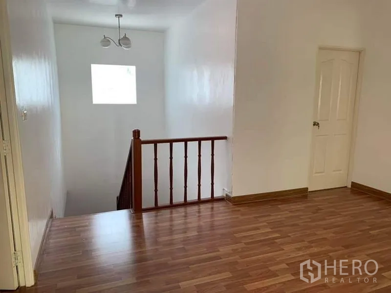 Detached House for sale in Sai Mai, Bangkok - Upper landing with wooden stair railing, laminate floors and a white door.