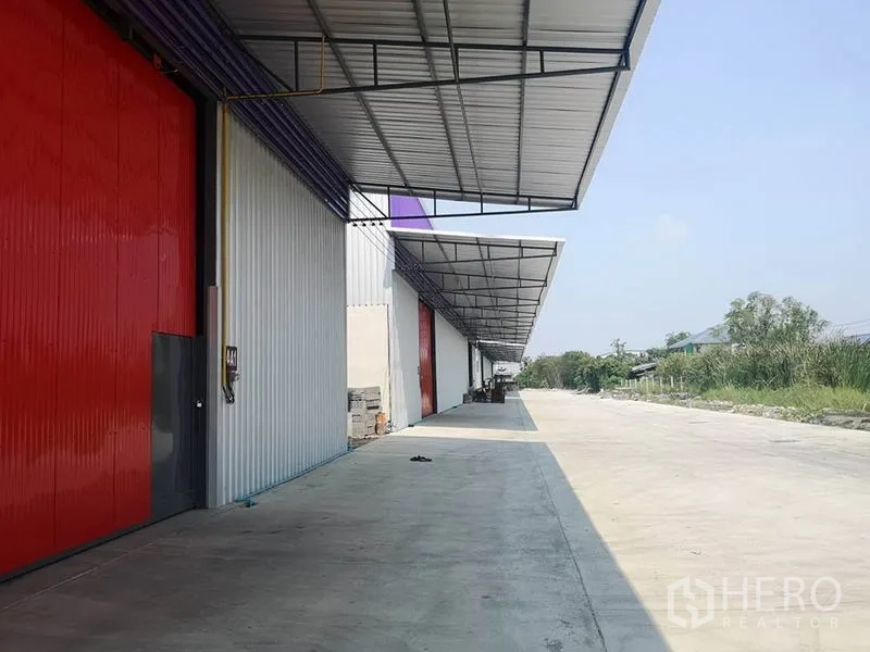 Warehouse for rent in Sai Mai, Bangkok - Exterior loading bay with continuous canopies, multiple red doors and a wide truck-friendly driveway.