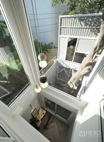 Townhouse for rent in Watthana, Bangkok - Double-height atrium with floor-to-ceiling windows, pendant lights and view to a tree-filled courtyard.