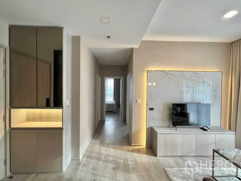 Condominium for rent in Watthana, Bangkok - Modern living room with marble accent wall, TV console and hallway leading to bedroom.