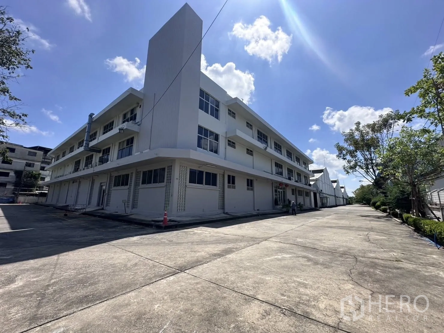 Warehouse for rent in Mueang Samut Prakan, Samut Prakan - Corner view of a three‑storey office building next to a row of warehouses on a sunny day.