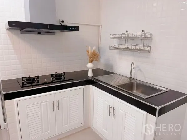 Townhouse for rent in Huai Khwang, Bangkok - Modern L-shaped kitchen with gas hobs, hood, sink and white storage cabinets.
