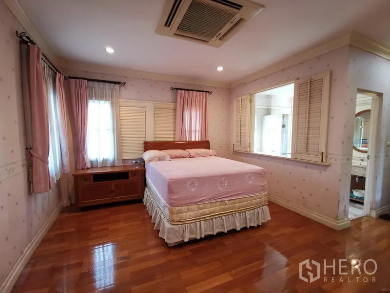 独立式住宅 出售在Phra Khanong, Bangkok - 温馨卧室，粉色窗帘、双人床与木地板，连通套内卫浴的窗户。