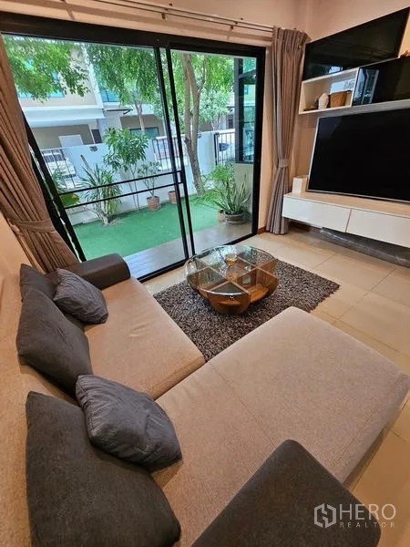 独立式住宅 出租在Bang Phli, Samut Prakan - 客厅L型沙发，落地推拉门通向花园与电视柜