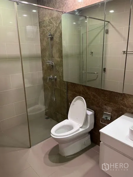 Detached House for rent in Wang Thonglang, Bangkok - Modern bathroom featuring a glass-enclosed shower, toilet, and mirrored storage cabinet.
