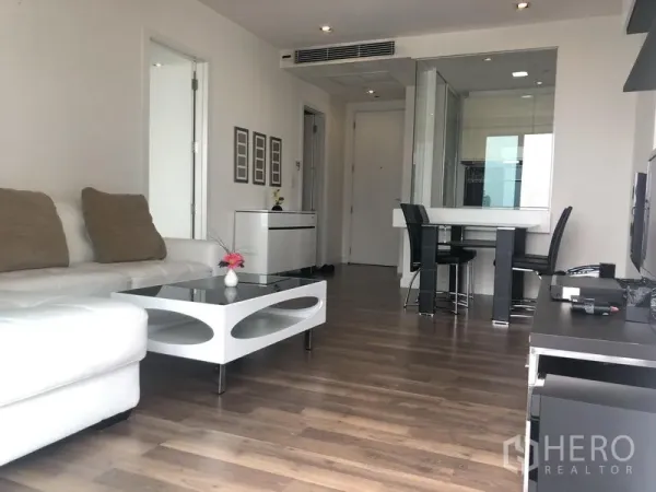 Condominium for rent or sale in Phra Khanong, Bangkok - Bright living room with white L-shaped sofa, modern coffee table, wood floors, and a dining area in a Bangkok condo.