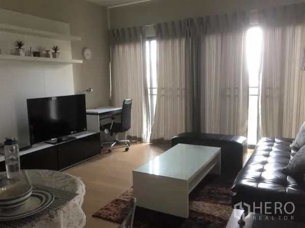Condominium for rent in Watthana, Bangkok - Bright Ekkamai condo living room with tall windows, work desk, TV unit and leather sofa.