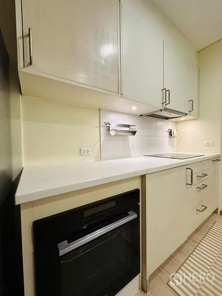 Condominium for rent in Bang Rak, Bangkok - Modern galley kitchen with white cabinets, built-in oven, and induction cooktop.