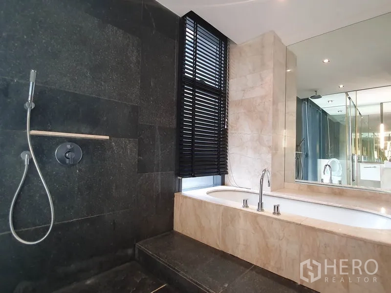 Condominium for rent in Sathon, Bangkok - Bathroom with soaking bathtub, separate shower, dark stone wall and large mirror.