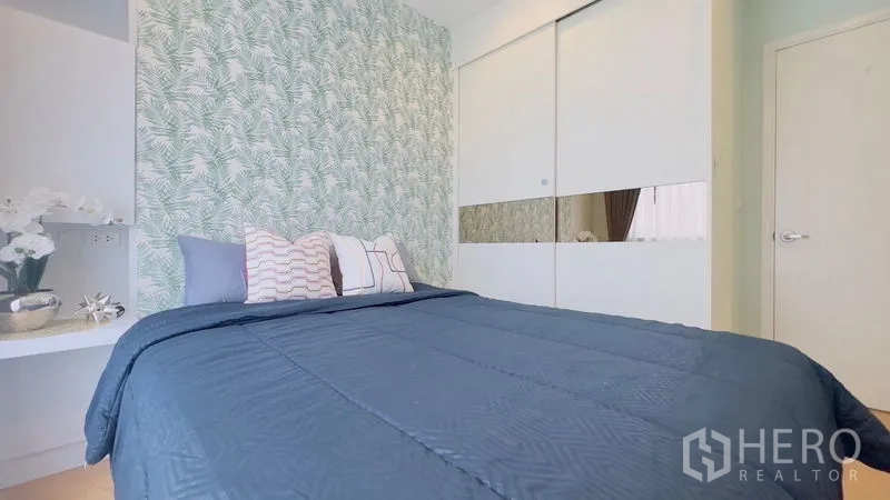 Condominium for rent in Watthana, Bangkok - Cozy bedroom with patterned accent wall, blue bedding and sliding wardrobe.