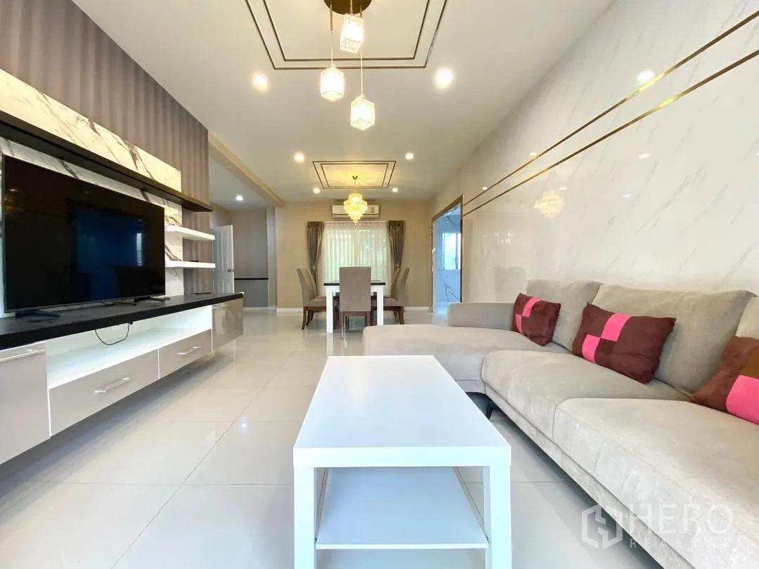 独栋房屋 for rent in Suan Luang, Bangkok - 明亮客厅，L形沙发、电视墙与亮面地砖。