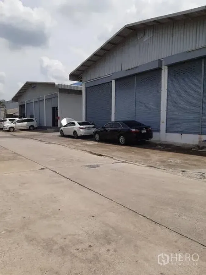 Warehouse for rent in Bang Phli, Samut Prakan - Row of warehouse buildings with shutter doors along a wide concrete road.