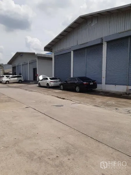 Warehouse for rent in Bang Phli, Samut Prakan - Row of warehouse buildings with shutter doors along a wide concrete road.