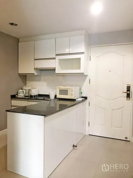 Condominium for rent or sale in Khlong Toei, Bangkok - Entry kitchenette with white cabinets, black countertops and microwave.