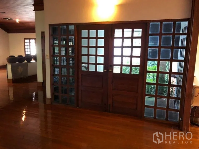 Detached House for sale in Bang Na, Bangkok - Wooden double doors with grid glass panels opening toward greenery.