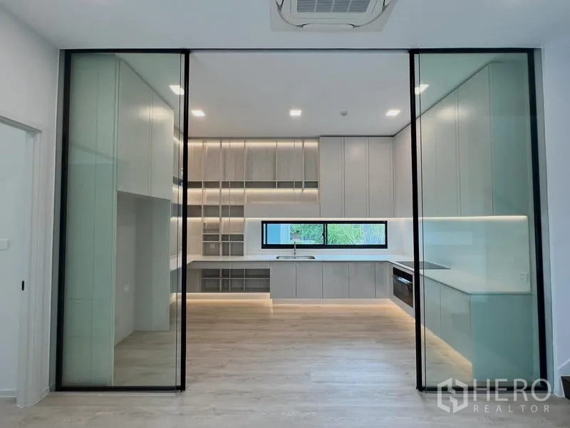 Detached House for rent or sale in Saphan Sung, Bangkok - Kitchen viewed through wide sliding glass partitions with LED accent lighting.