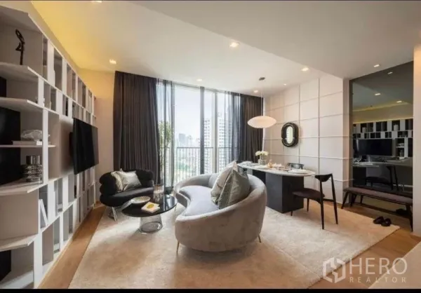 Condominium for rent in Watthana, Bangkok - Contemporary living room with a curved sofa, wall shelving, dining nook, and balcony facing the skyline.