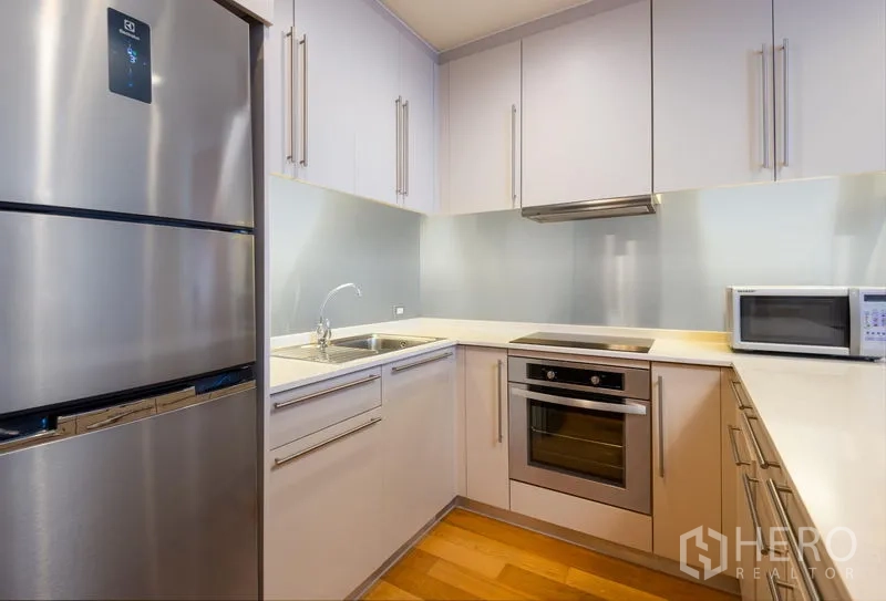 Condominium for rent in Bang Kho Laem, Bangkok - U‑shaped modern kitchen featuring oven, cooktop, microwave and generous storage.