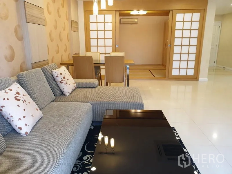 公寓 出租在Watthana, Bangkok - 客厅配转角沙发与黑色茶几、餐桌，并有和风推拉门通往多功能房。