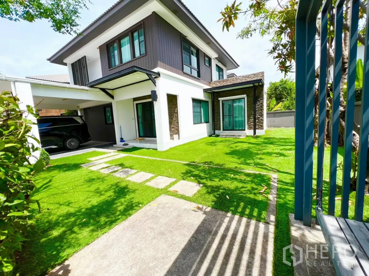 บ้าน ให้เช่าหรือขายในBang Phli, Samut Prakan - สนามหญ้าด้านข้างรับแดด ทางเดินแผ่นหิน และที่จอดรถมีหลังคาข้างตัวบ้าน.