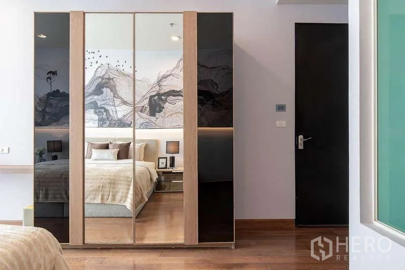 Condominium for rent in Pathum Wan, Bangkok - Bedroom wardrobe with mirrored doors reflecting the bed and artwork.