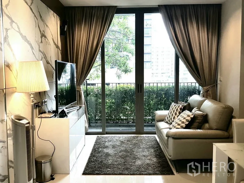 Condominium for rent in Sathon, Bangkok - Living area with sofa, TV cabinet and sliding glass doors to balcony greenery.