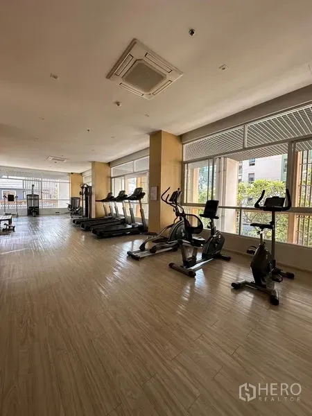 Apartment for rent in Khlong Toei, Bangkok - Resident fitness room with treadmills and stationary bikes beside wide windows.