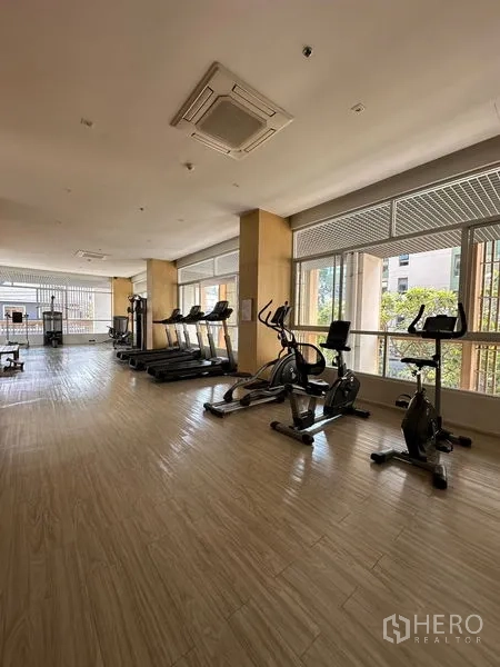 Apartment for rent in Khlong Toei, Bangkok - Resident fitness room with treadmills and stationary bikes beside wide windows.