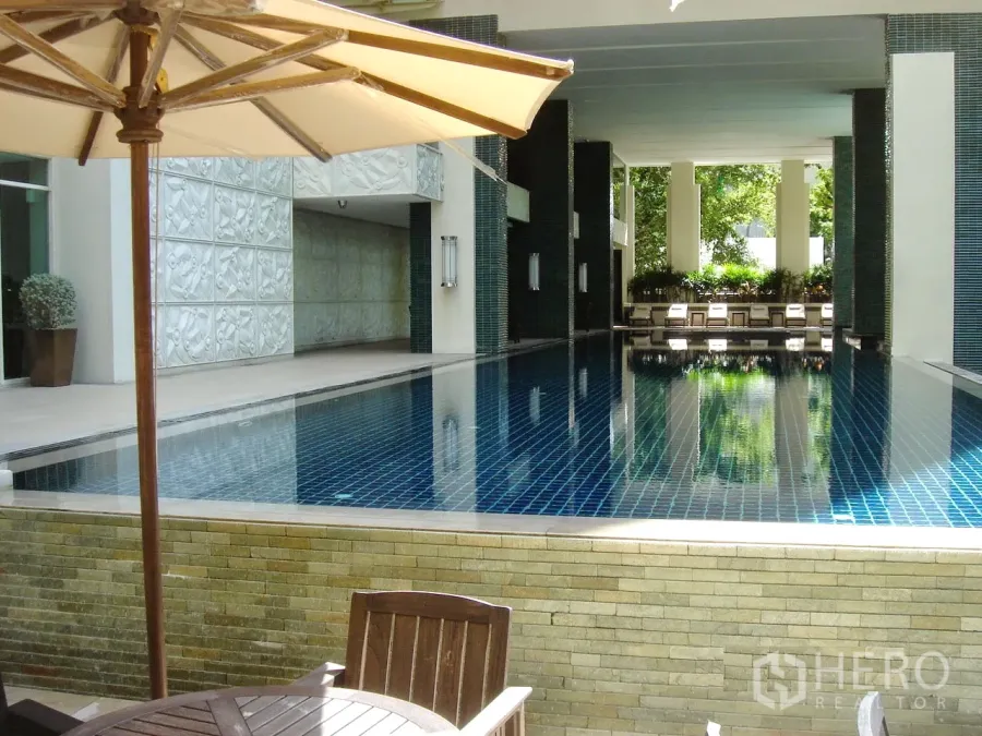 公寓 出售在Pathum Wan, Bangkok - 豪华公寓的室内泳池与躺椅和遮阳伞，蓝色池砖。