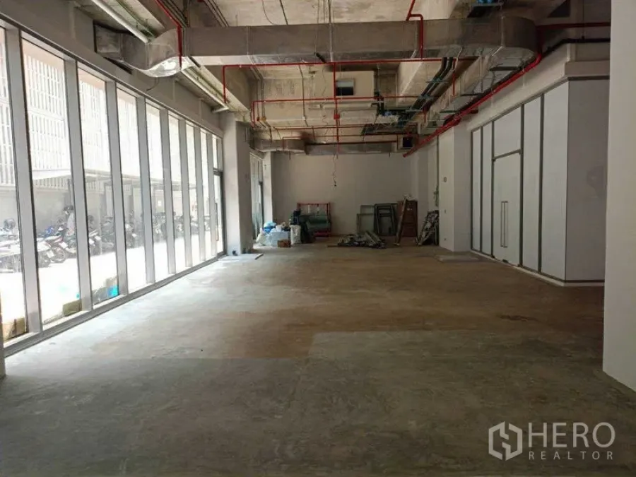 Retail Space for rent in Watthana, Bangkok - Long storefront interior with wall‑length glass panels and raw concrete floor, ideal for a showroom or cafe.