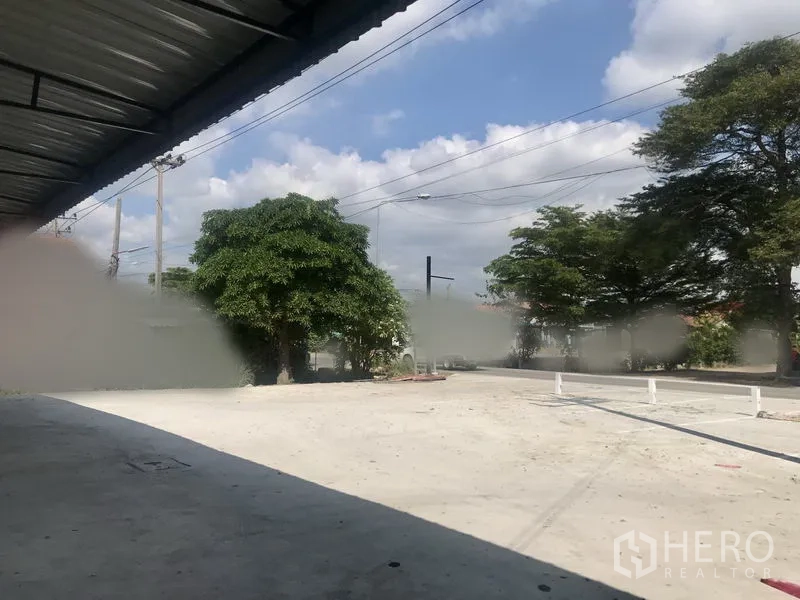货栈 出租在Lam Luk Ka, Pathum Thani - 宽阔前场与临街出入口，路边树木与电线杆。