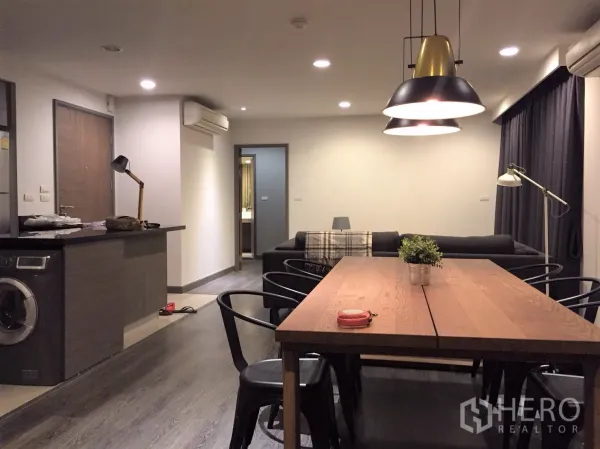 公寓 出租或出售在Watthana, Bangkok - 开放式客餐厅，木地板，长餐桌与吊灯，带洗衣机的厨房台面和沙发通向卧室。
