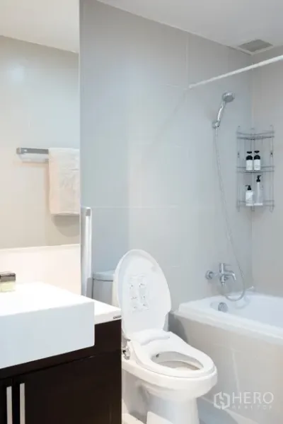 Condominium for rent in Khlong Toei, Bangkok - Modern bathroom with bathtub, shower, white tiles and vanity cabinet.