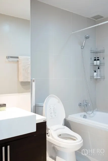 Condominium for rent in Khlong Toei, Bangkok - Modern bathroom with bathtub, shower, white tiles and vanity cabinet.
