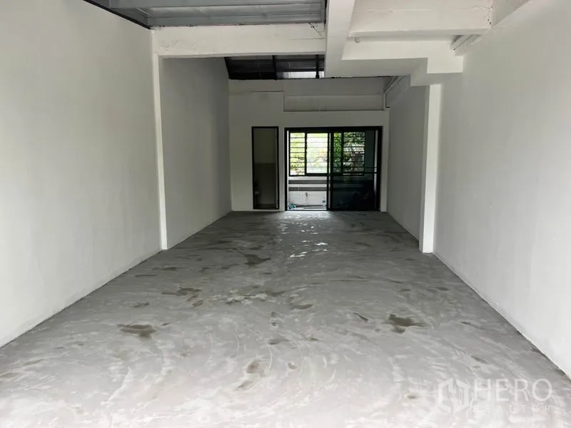 零售空间 出租在Watthana, Bangkok - 45㎡毛坯商铺，白色墙面、高挑层高、混凝土地面，后侧设窗户与卫生间门。