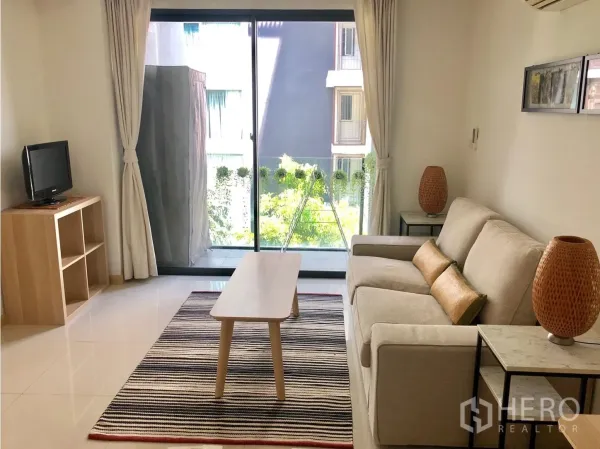 公寓 出租在Watthana, Bangkok - 明亮客厅，沙发与地毯，落地移门通向带绿景的阳台。