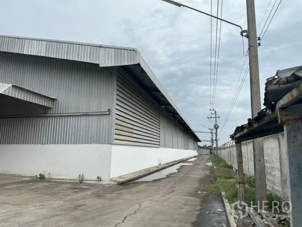Factory for rent in Lat Lum Kaeo, Pathum Thani - Metal‑clad factory exterior with service driveway, power poles and perimeter wall in Pathum Thani.