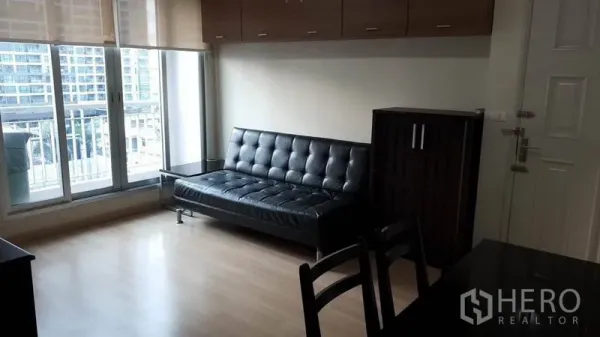 Condominium for rent in Bang Rak, Bangkok - Bright living room with black leather sofa, large windows, city view and wood floors in a Bang Rak condo.