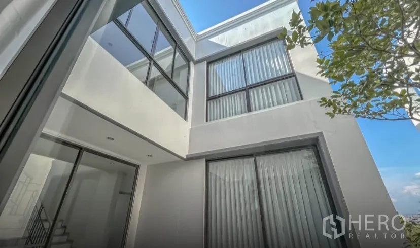 Detached House for rent or sale in Lat Krabang, Bangkok - Modern three‑storey detached house courtyard with large windows and blue sky in Lat Krabang, Bangkok