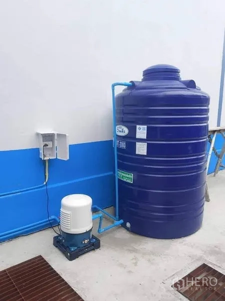 Warehouse for rent in Bang Phli, Samut Prakan - Large blue water storage tank with electric pump installed beside the warehouse wall.
