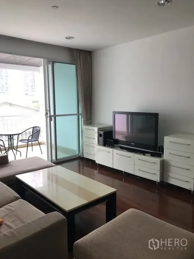 Condominium for rent in Khlong Toei, Bangkok - Living room with L-shaped sofa, TV unit, and sliding glass door opening to a balcony.