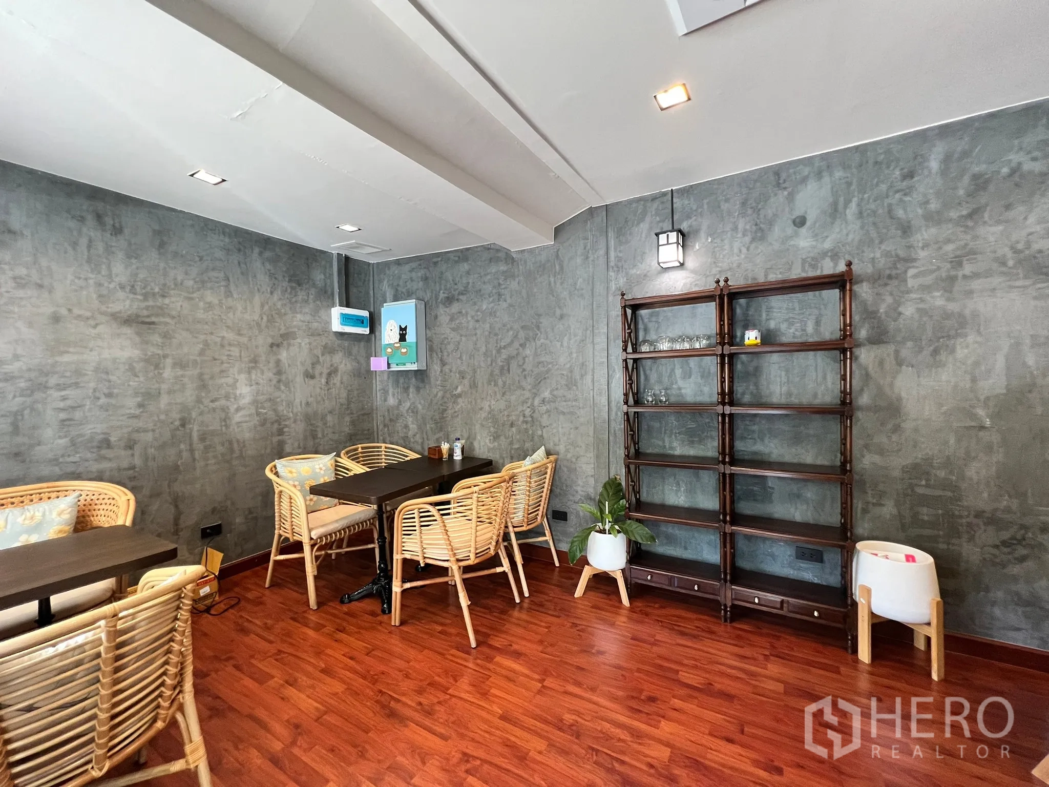 พื้นที่ขายปลีก ให้เช่าในWatthana, Bangkok - มุมนั่งเล่นอบอุ่น เก้าอี้หวาย ผนังคอนกรีตขัดมัน พื้นไม้ และชั้นวางของ