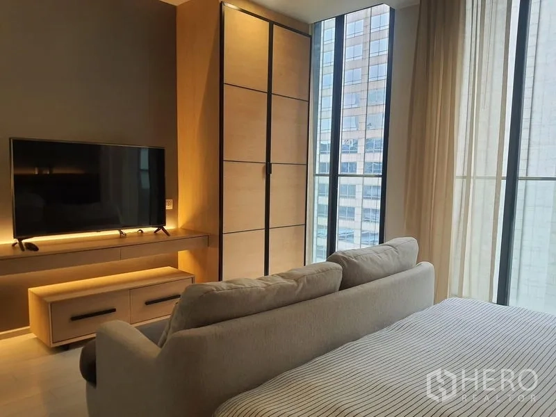 公寓 出租在Pathum Wan, Bangkok - 转角卧室设衣柜、电视与落地窗，可欣赏城市景观。
