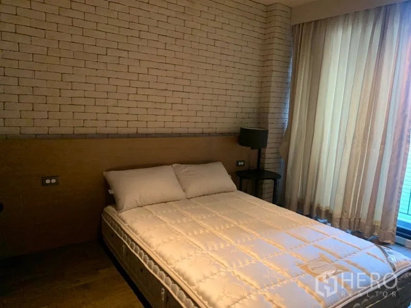 公寓 出租在Watthana, Bangkok - 温馨卧室，砖纹特色墙、纱帘与床头灯。